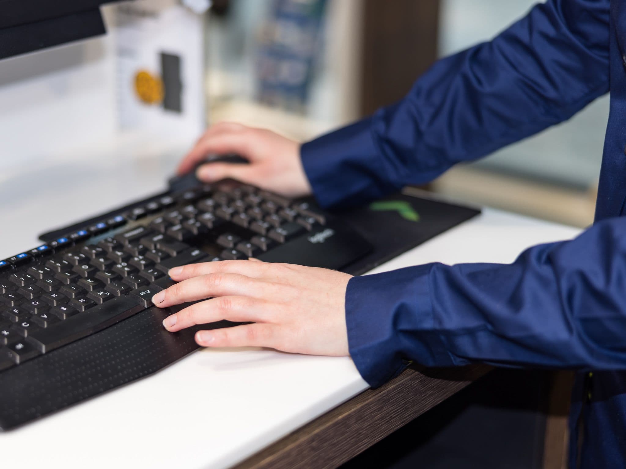 Person's hands on a black keyboard and mouse on a white desk.