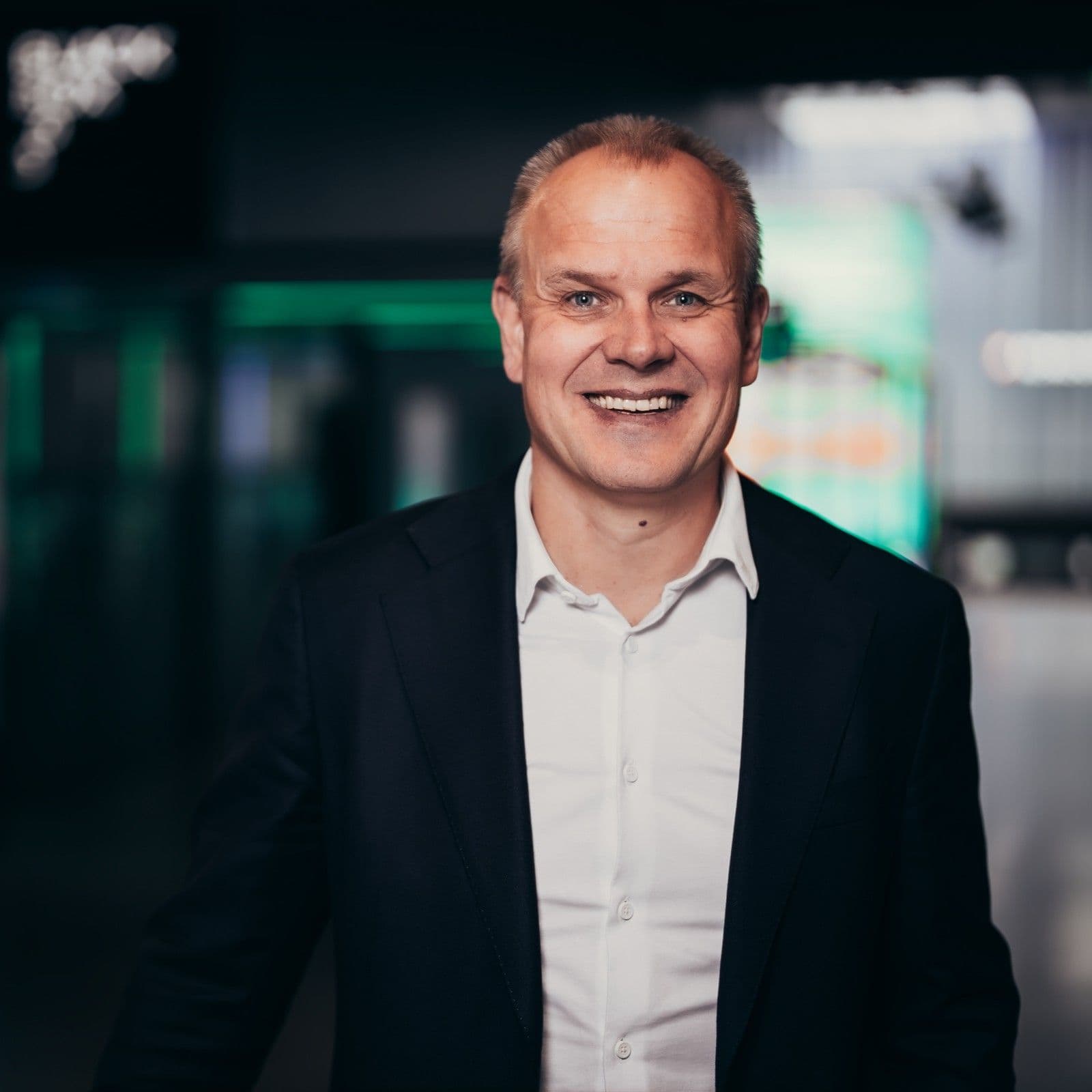 A smiling bald man in a navy blue shirt with a green logo.